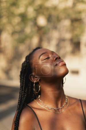 Téléchargez les photos : Portrait d'une jeune femme noire avec des tresses dans les cheveux inspirant et relaxant avec les yeux fermés, fond flou - en image libre de droit