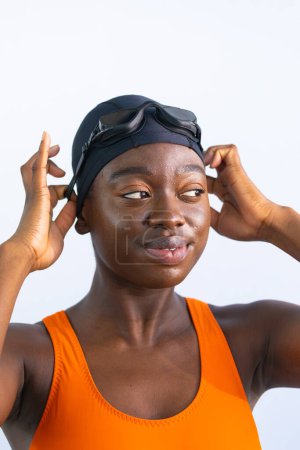 Photo for Portrait of a black young woman smiling while adjusting her swim goggles and plain white background - Royalty Free Image