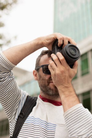 Téléchargez les photos : Un jeune homme, un voyageur, prenant des photos avec un appareil photo numérique, dans la rue, dans une ville en Espagne. - en image libre de droit