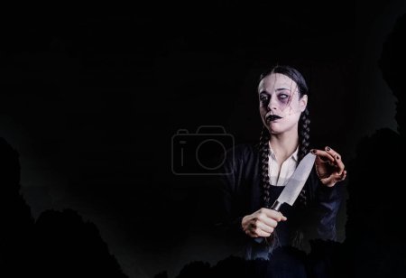 Foto de Una mujer con trenzas largas, de aspecto gótico y oscuro, juega con un cuchillo de carnicero con la mano, en un ambiente espeluznante y espeluznante, perfecto para halloween - Imagen libre de derechos