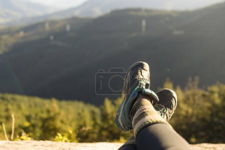 Téléchargez les photos : Détail des bottes d'un randonneur, depuis le sommet d'une montagne, avec le paysage naturel hors foyer en arrière-plan - en image libre de droit