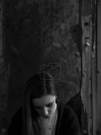 Photo for A young woman looks down, as if depressed or sad, in an environment that seems abandoned and dark - Royalty Free Image