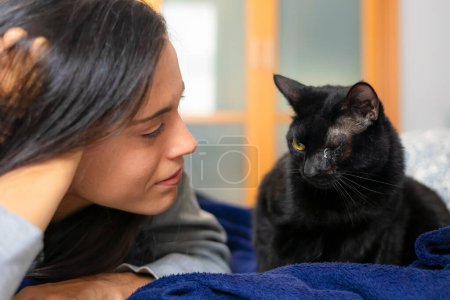 Téléchargez les photos : Une jeune femme regarde avec amour son chat noir au lit alors qu'elle se réveille le matin. - en image libre de droit