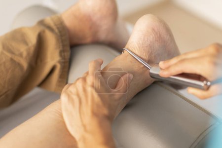 Téléchargez les photos : Un homme plus âgé est traité dans une clinique de physiothérapie avec une technique de fibrolyse diacutanée et à crochet dans la région du pied et de la cheville - en image libre de droit