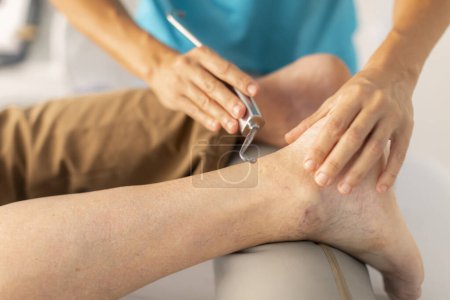 Téléchargez les photos : Un homme plus âgé est traité dans une clinique de physiothérapie avec une technique de fibrolyse diacutanée et à crochet dans la région du pied et de la cheville - en image libre de droit