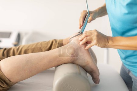 Photo for An older man is treated in a physiotherapy clinic with a hook and diacutaneous fibrolysis technique in the foot and ankle area - Royalty Free Image