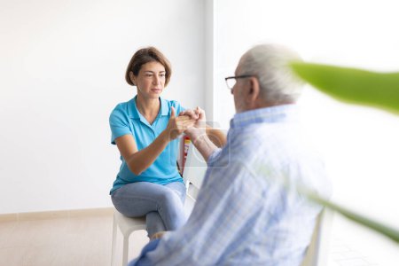 Photo for A physiotherapist talks to her patient, an older man, while examining his hand and arm for injuries - Royalty Free Image