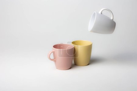 Photo for Fantasy mockup of three coffee cups, one of them flying in the air, colorful, pink, yellow and white, on a plain background - Royalty Free Image