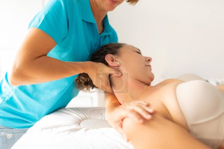 Téléchargez les photos : Une physiothérapeute effectue un exercice d'étirement sur le cou et l'épaule de sa patiente - en image libre de droit