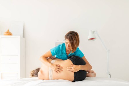 Photo for A female physical therapist performs a stretching and pressure exercise on her patient's lower back - Royalty Free Image