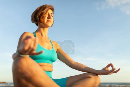Foto de Una mujer realiza ejercicios de meditación en la playa, después de una sesión de Pilates al atardecer - Imagen libre de derechos