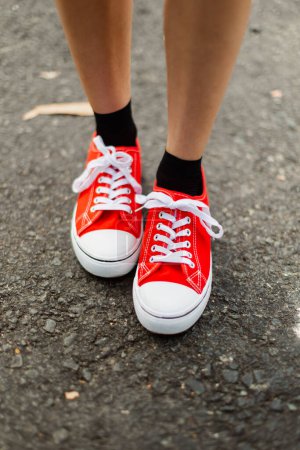 Téléchargez les photos : Les pieds d'une jeune fille, portant des chaussures à bout en caoutchouc blanc rouge sur l'asphalte d'une route - en image libre de droit