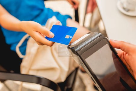 Téléchargez les photos : Une jeune fille paie avec une carte de crédit sans contact sur une machine de carte de crédit après avoir pris un café - en image libre de droit
