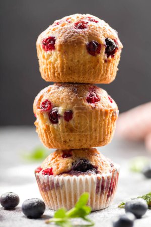 Freshly baked muffins with powdered sugar and fresh berries. Homemade muffins with fresh blueberries and raspberries on a light background. Homemade baking concept. Soft focus