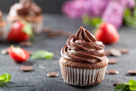 Photo for Chocolate cupcakes. Freshly baked homemade cupcakes with strawberries, mint leaves and lilac flowers on a gray background. Home baking concept. Soft focus - Royalty Free Image