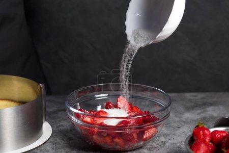 Téléchargez les photos : Le sucre est versé dans les fraises sur un fond sombre - en image libre de droit