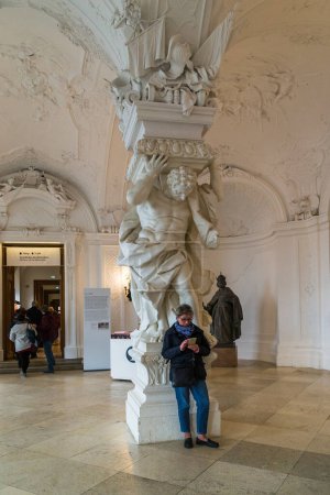 Foto de VIANNA, AUSTRIA - 16 DE MAYO DE 2019: Se trata de un visitante no identificado en una de las columnas con un atlas en el vestíbulo del Palacio del Belvedere Superior. - Imagen libre de derechos