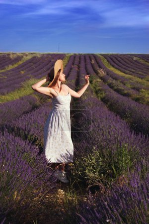 Foto de Una hermosa chica en un vestido de verano y sombrero se encuentra en el fondo de un campo de lavanda. Pastoral. Retrato vertical de cuerpo entero - Imagen libre de derechos