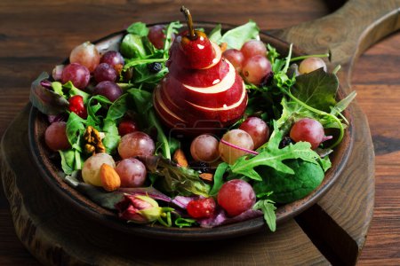 Téléchargez les photos : Salade lumineuse et savoureuse avec poire rouge, raisin, roquette, noix et fruits secs sur une assiette brune - en image libre de droit
