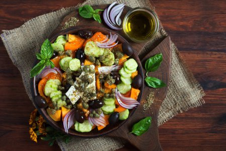 Photo for Classic Greek salad with yellow tomatoes, cucumbers, olives, capers and soft cheese on a dark wooden surface - Royalty Free Image