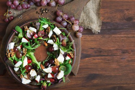 Téléchargez les photos : Salade avec un mélange d'herbes, poires, raisins, fromage blanc, noix et fruits secs sur une assiette brune - en image libre de droit
