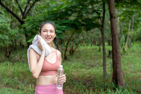 Photo for Young attractive Asian woman wiping off her sweat from her forehead during her water break from her morning exercise run at a running track of a local park - Royalty Free Image