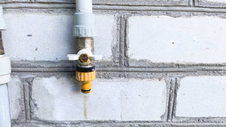 water tap on the street with a bright yellow switch, against the background of a brick wall