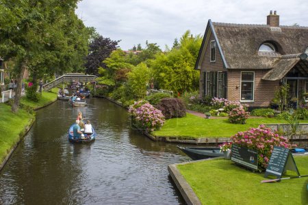 GIETHOORN, NETHERLANDS - AUGUST 01 2017: Unknown visitors in the sightseeing boating trip in a canal in Giethoorn. The beautiful houses and gardening city is know as "Venice of the North".