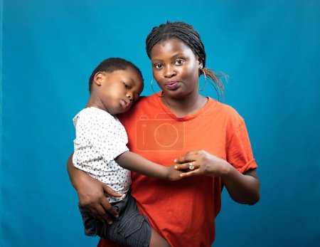 Foto de Una madre, tía o tutora africana feliz cuidando a un niño pequeño mientras lo lleva en sus manos y también mirando a la cámara - Imagen libre de derechos