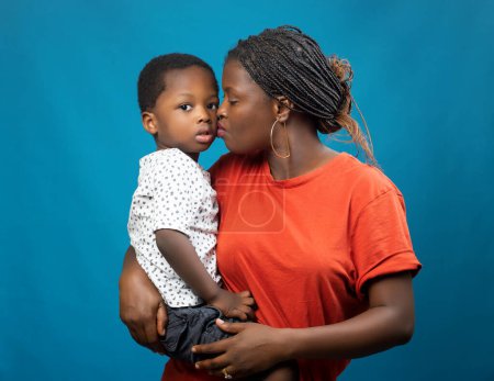 Foto de Una madre, tía o tutor africano feliz llevando a un niño varón y besándolo en la mejilla - Imagen libre de derechos