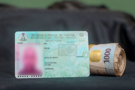Téléchargez les photos : Nigerian voter's card placed with a rolled naira notes, cash or money, depicting illegally vote buying during elections in Nigeria - en image libre de droit