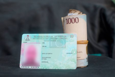 Téléchargez les photos : Nigerian voter's card placed with a rolled naira notes, cash or money, depicting illegally vote buying during elections in Nigeria - en image libre de droit