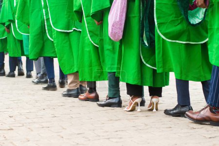 Téléchargez les photos : Alignement des étudiants diplômés universitaires portant leur tenue de fin d'études vertes et marchant vers la salle de réception de l'école pour leur cérémonie de remise des diplômes au Nigeria - en image libre de droit
