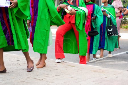 Foto de Conjunto de estudiantes universitarios graduados con su atuendo de graduación verde y marchando hacia la sala de recepción de la escuela para su ceremonia de desmayo en Nigeria - Imagen libre de derechos