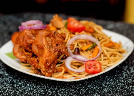Foto de Un plato delicioso surtido de fideos espagueti y carne de pollo, adornado con cebollas y tomates en rodajas, entre otros ingredientes de alimentos y especias cocinadas en Nigeria - Imagen libre de derechos