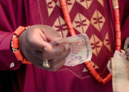 Photo for A yoruba groom from Nigeria holding a hundred Naira Nigerian cash or money in his hand during a traditional wedding engagement ceremony - Royalty Free Image