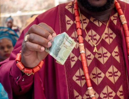 Téléchargez les photos : Un marié yoruba du Nigeria tenant dans sa main une vingtaine d'argent ou d'argent nigérian Naira lors d'une cérémonie traditionnelle de fiançailles de mariage - en image libre de droit