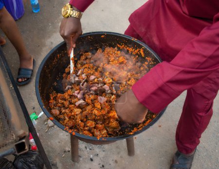 Photo for Hands of an African man, chef or caterer stirring together seasoned goat meats in a cooking pot during a party in Nigeria - Royalty Free Image