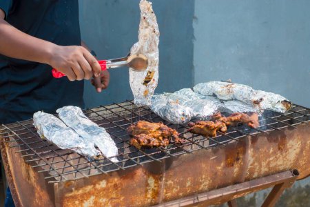 Téléchargez les photos : Un chef de grill ou de barbecue, griller et faire griller du poisson enveloppé dans du papier d'aluminium d'argent lors d'un événement de fête en plein air au Nigeria - en image libre de droit