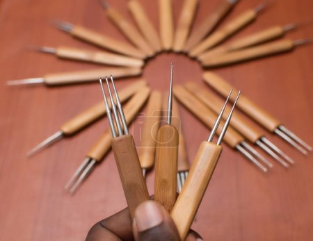 Téléchargez les photos : Une main africaine tenant trois outils de crochet de cheveux en bois tandis que d'autres peuvent être vus affichage sur une table dans un salon et boutique de vente d'entreprise de mode au Nigeria - en image libre de droit
