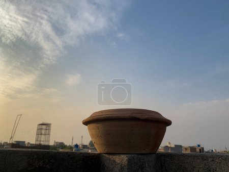 Photo for Mud water pot placed on the top of roof wall. Bird water feeder utensils with sunlight and a cloudy sky in the background. - Royalty Free Image