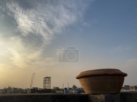 Photo for Mud water pot placed on the top of roof wall. Bird water feeder utensils with sunlight and a cloudy sky in the background. - Royalty Free Image