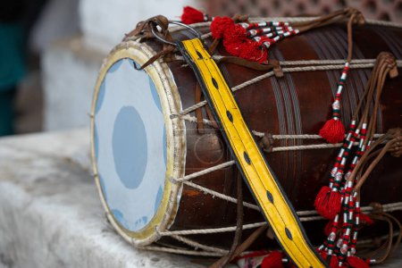 Traditionelles Trommel oder Dhol-Instrument mit gelbem Band und roten Blumen auf dem Boden. 