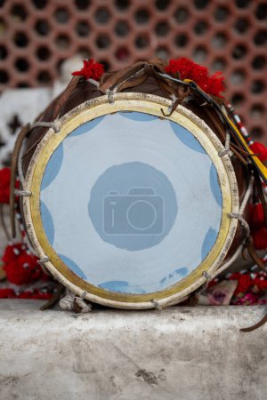 Instrumento tradicional de tambor o dhol con banda amarilla y flores rojas colocadas en el suelo. 