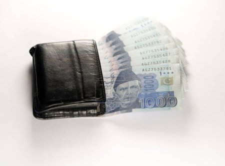 Foto de Mil billetes de 1000 rupias alineados con una cartera de cuero negro. Paquistán Banco de Estado billetes de moneda oficial 2024 aislados en un fondo blanco. - Imagen libre de derechos