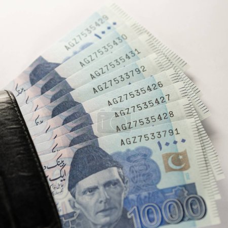 Mil billetes de 1000 rupias alineados con una cartera de cuero negro. Paquistán Banco de Estado billetes de moneda oficial 2024 aislados en un fondo blanco.