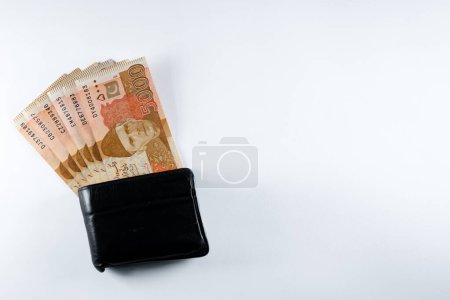 Five thousand 5000 rupee bank notes aligned with a black leather wallet. Pakistan State Bank official currency notes 2024 isolated on a white background.