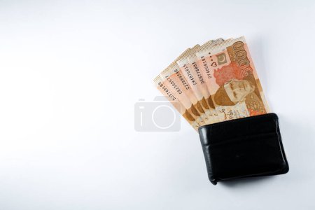 Cinco mil billetes de 5000 rupias alineados con una cartera de cuero negro. Paquistán Banco de Estado billetes de moneda oficial 2024 aislados en un fondo blanco.