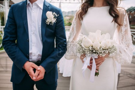 Photo for The groom in a blue suit and the bride in a white dress with a bouquet in their hands. Wedding composition for your design or creative illustrations. - Royalty Free Image