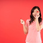 Happy beautiful Asian woman feel romance holding small little heart isolated over red background. Valentines Day concept.